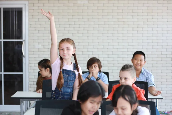 Menina bonito no vestido rosa levantando as mãos em sala de aula com o rosto feliz (conceito de educação ) — Fotografia de Stock