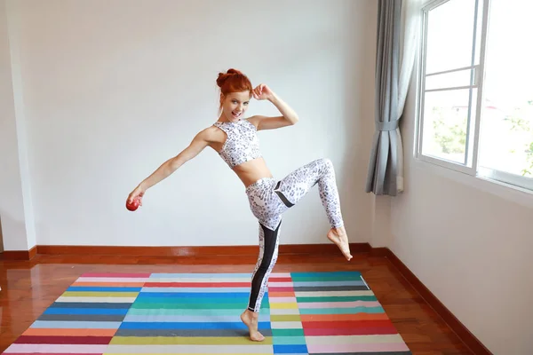 Retrato de joven atractiva mujer caucásica en ropa deportiva en blanco y negro que baila con música mientras sostiene manzana en el dormitorio con cara feliz y sonriente —  Fotos de Stock