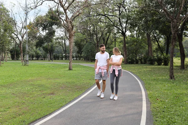 年轻的白种人夫妇谁穿运动服是爱。在夏季，拥抱和步行在公园 — 图库照片
