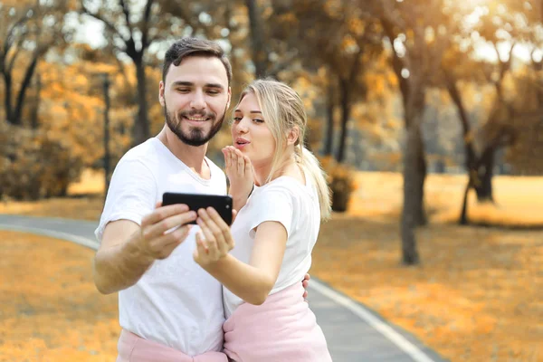 年轻夫妇在爱用手机一起，给吻智能手机在公园（假期或技术概念) — 图库照片