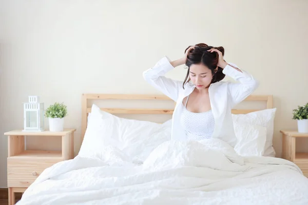 白いシャツを着て陽気でセクシーなアジアの若い女性は、朝目を覚ますとリラクゼーションと幸せな顔で寝室のベッドに座ってストレッチ — ストック写真