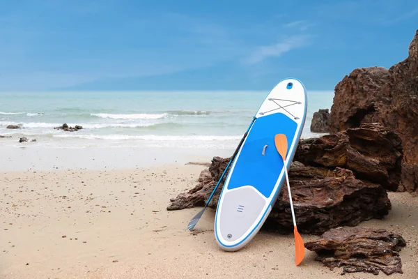 Fehér és kék szörfdeszka a homokos strandon, kék tengeri és égbolt háttérrel — Stock Fotó