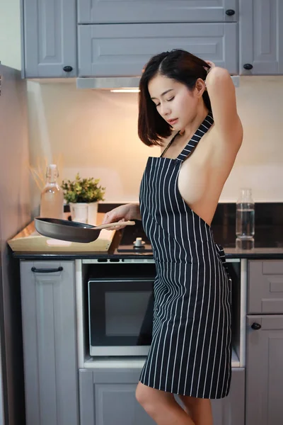 黒と白のセクシーなエプロンでセクシーで魅力的なアジアの女性の妻の半分の長さ、リラクゼーションと休日に笑顔でキッチンで調理しながらブラジャーなし(ライフスタイルコンセプト) — ストック写真