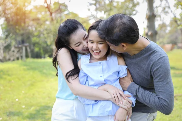 Bild av lycklig familj, dotter sätta händerna på föräldrarna kind med leende medan far och mor kysser under sommaren i parken — Stockfoto