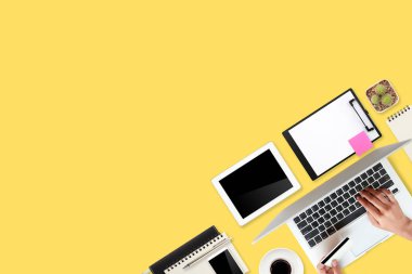 Düz çalışma masası dizüstü bilgisayarı, ofis malzemeleri, kahve fincanı, tablet ve cep telefonu sarı pastel arka planda.