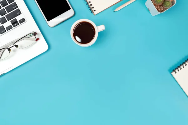 Business Office stół z przestrzenią roboczą, laptop, filiżanka do kawy, Notatnik, ołówek, roślina i telefon komórkowy na niebieskim tle pastelowych — Zdjęcie stockowe