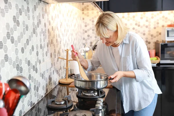 Kaukasische ältere Frau, die während ihres Rentnerlebens und glücklichen Urlaubs Essen in der Küche zubereitet — Stockfoto