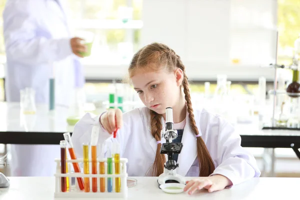 Curiosa niña está experimentando la ciencia mediante la caída de líquido en el tubo de ensayo con microscopio y la cara de atención (concepto de educación y científico ) —  Fotos de Stock