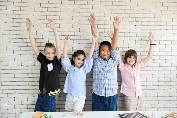 Grupp av multietniska internationella skolan barn att höja händerna i klassrummet med Happy Face med White Wall (utbildning Concept) — Stockfoto