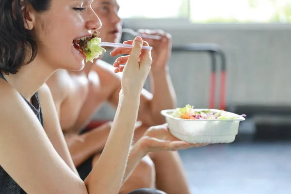 Close up schöne kaukasische Paar Fitness Mann und Frau machen eine Pause und essen Salat in der Turnhalle nach dem Fitnesstraining mit glücklich lächelndem Gesicht — Stockfoto