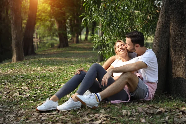年轻的夫妇在爱，坐在和拥抱在公园在夏季与树木（友谊或情人节的概念) — 图库照片