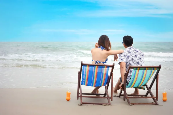 Vista trasera de en amor pareja asiática que lleva traje de baño sentado en la silla de cubierta en la playa tropical con naranja y hermoso jugo de cielo azul en vacaciones de vacaciones durante el tiempo feliz en verano — Foto de Stock