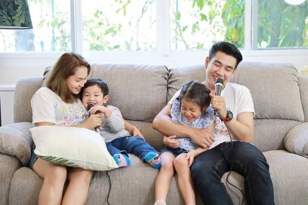 Szczęśliwa azjatycka rodzina, ojciec, matka córka i syn śpiewający karaoke na kanapie w salonie ze szczęśliwą uśmiechniętą twarzą (koncepcja relaksu i technologii) — Zdjęcie stockowe