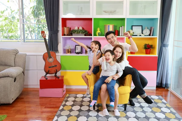 Happy asian family father, mother, son and daughter raising hands up with happy smiling face on grey sofa in living room — Stock Photo, Image
