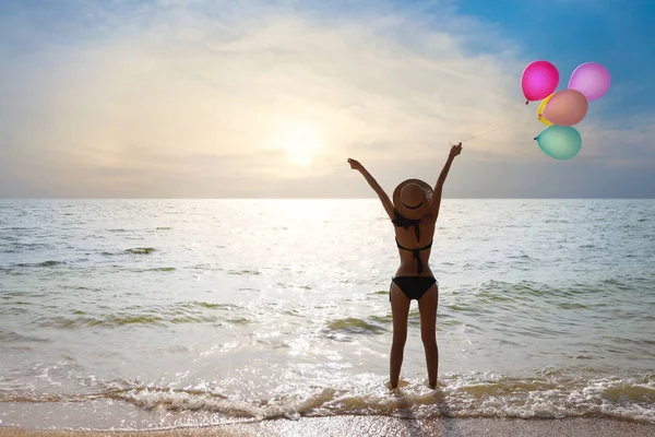 Felicidad en vacaciones silueta espalda ver imagen de joven asiático hermosa y sexy chica en bikini negro que de pie y sosteniendo globos y levantar la mano con cara feliz y sonrisa en la puesta de sol en las vacaciones de verano — Foto de Stock