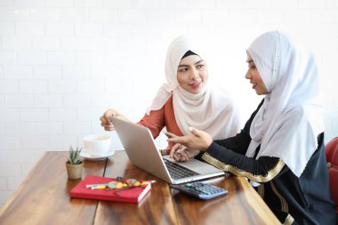 Yeni nesil iş kadını Müslümanlar kafeteryada buluşuyorlar, ellerinde bilgisayar ve masa başında kahve fincanı var.