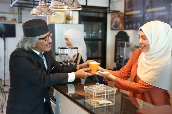 muslim customer businessman wearing black suit receive a cup of coffee from young muslim barista girls at coffee shop counter