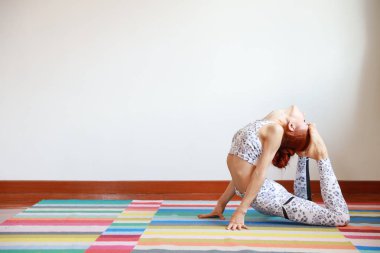 Siyah-beyaz spor kıyafetleri içinde yoga yapan ya da evde yoga yapan beyaz bir kadının yan görüntüsü. Beden ve zihinsel denge. (sağlıklı yaşam konsepti)