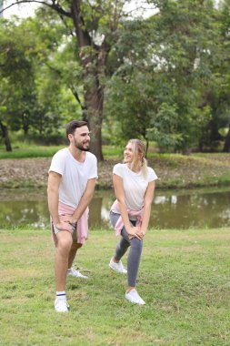 Kafkasyalı genç bir çiftin yaz mevsiminde parkta yüzleri gülen ve yeşil ağaçlarla egzersiz ve esneme zevkini çıkardığı görüntüsü.