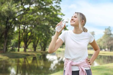 parkta duran beyaz spor giyen genç güzel beyaz kadın. o gülme ve mutlu gülümseyen yüz ile saf su içerken zevk