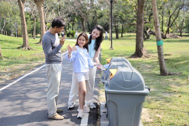 Parkta mutlu Asyalı aile grubu, veliler elleri ok sembolü anlamı ile çöpe boş plastik şişe atmak için çocuklara öğretmek ya da gülümseyen yüzü ile Iyi iş