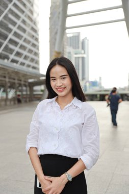 ön görünüm genç yetişkin asyalı iş kadını, kırmızı dudak ve beyaz üniformalı uzun saçlı güzellik yüzü kamera ve gülümseme bakarak şehir arka plan ile açık havada ayakta