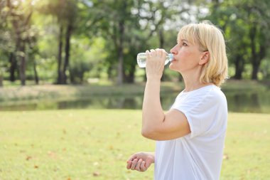 beyaz gömlek tutan ve içme suyu şişesi giyen yaşlı beyaz kadın. tatillerde ferahlatıcı 
