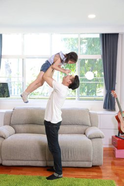 tam uzunlukta mutlu asyalı baba o gülümseyen yüzü (yaşam tarzı kavramı ile oturma odasında ayakta iken kızını atar)