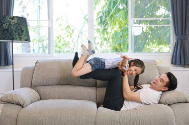 mutlu asyalı baba o gülümseyen yüzü (yaşam tarzı kavramı ile oturma odasında gri kanepe üzerinde yatarken kızını atar)