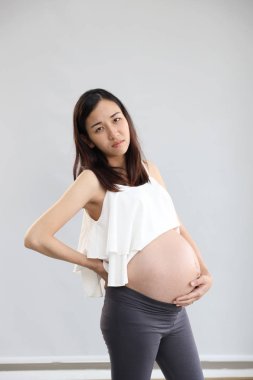 genç hamile asyalı kadın ayakta ve beyaz arka plan üzerinde midesini tutarak başka bir el vurguladı