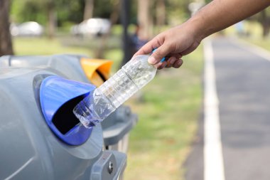 yakın adam el yeşil ağaç bulanık arka plan ile güneşli bir günde parkta çöp içine boş plastik şişe atmak