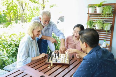 Sunny Day 'de mutlu bir gülümsemeyle satranç tahtası oynayan bir grup çok ırklı yaşlı insanın yüksek açılı görüntüsü 