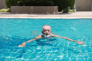 Emeklilik tatilinde havuzda yüzen mutlu, yaşlı, beyaz bir adam. Rahatlama ve gülümsemeyle.