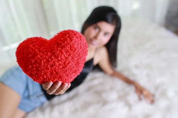 Beautiful and sexywoman lie down on bed with red heart in her hands — Stock Photo, Image