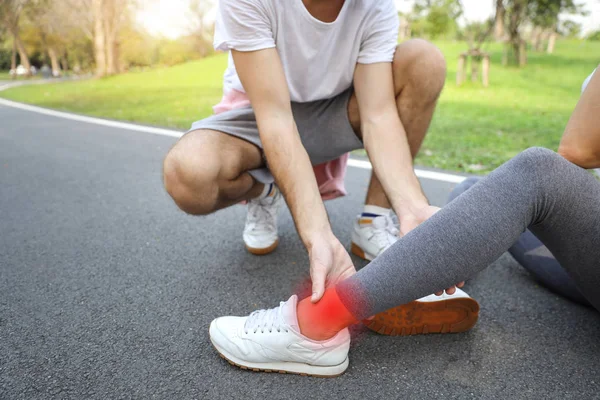 man helping jogger woman who hurt the ankle from too much exercise in the park