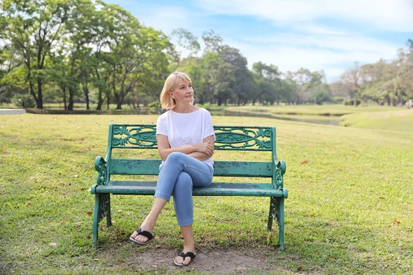 Старшая кавказская женщина в белом сидит в парке с отдыхом в летнее время — стоковое фото