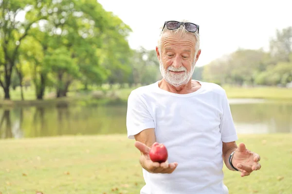 Älterer Mann mit Sonnenbrille und weißem Hemd hält im Sommer im Park einen Apfel in der Hand (gesundes Konzept)) — Stockfoto