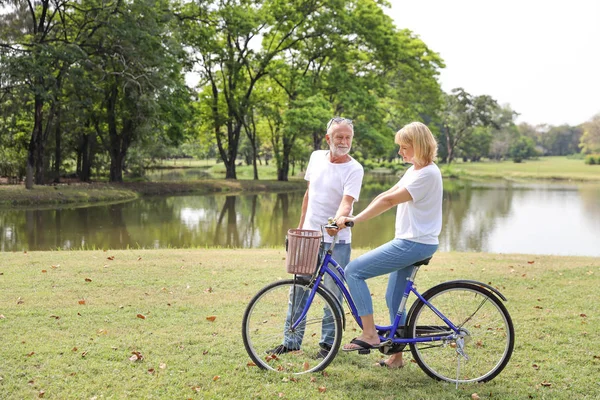 Старший мужчина и женщина катаются на велосипеде в парке в выходные дни с релаксацией и улыбкой лицо (старейший здоровой концепции ) — стоковое фото