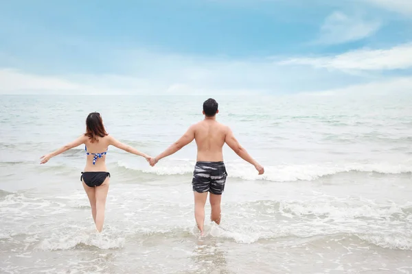 Vista posterior de la alegre pareja asiática con bikini o traje de baño. Se divierten mientras se toman de la mano y caminan o corren por la playa con amor en el día de luna de miel durante el verano — Foto de Stock