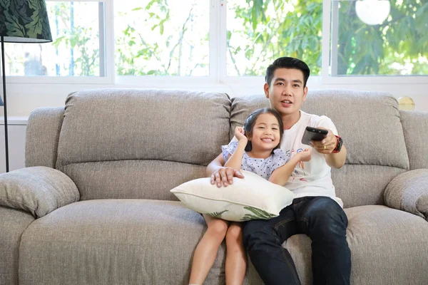 Happy Asian rodziny, ojciec i córka oglądają telewizję na kanapie w salonie i jest naciśnięcie pilota z uśmiechniętą twarzą (relaks i koncepcja technologii) — Zdjęcie stockowe