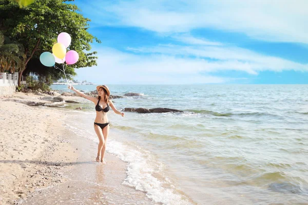 Felicidad en vacaciones imagen de joven asiático hermosa y sexy chica en bikini negro que sostiene globos y corriendo en la playa de arena con la cara feliz y sonrisa en el día soleado y la hora de verano — Foto de Stock