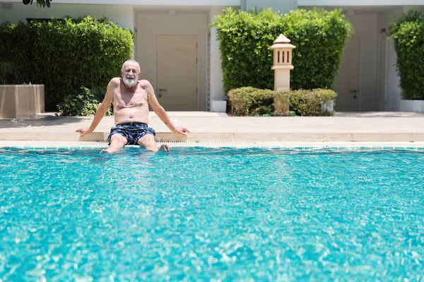 Feliz anciano caucásico tomar un descanso mientras se nada en la piscina durante las vacaciones de jubilación con la relajación y sonriendo — Foto de Stock