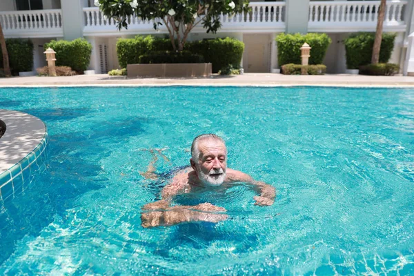 Feliz anciano caucásico nadar en la piscina durante las vacaciones de jubilación con la relajación y sonriendo — Foto de Stock