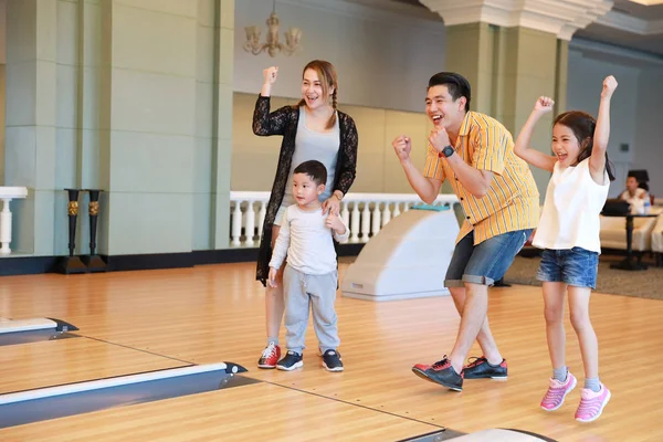 group of happiness asian family father, mother, son and daughter playing bowling in sport club with happy smiling face during holiday vacation