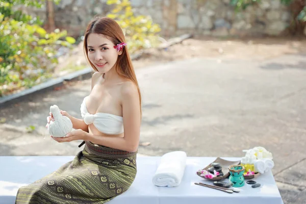 front view portrait young asian women, long hair with white dress sitting and holing herbal compresses for oil spa massage salon with happy smiling face and eyes contact