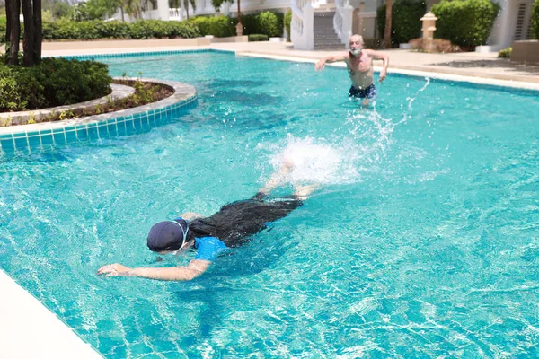 Счастливый пожилой кавказский муж и пожилая азиатская жена плавание в бассейне во время отдыха на пенсии с релаксацией и счастливо в солнечный день на открытом воздухе — стоковое фото