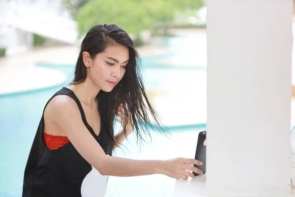 Çekici ve seksi Asyalı kız turuncu bikinili ve siyah takım elbiseli cep telefonunu canlı ya da güzel yüzle sohbet etmek için kullanmaya başlıyor. — Stok fotoğraf