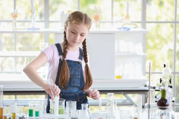 Curiosa niña está experimentando la ciencia con la cara de atención en tubo de ensayo colorido — Foto de Stock