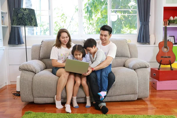 Happy Asian rodzina nauczania ich dzieci syna i córki, jak korzystać z komputera, siedząc na szarej kanapie w salonie z uśmiechniętymi twarzami — Zdjęcie stockowe