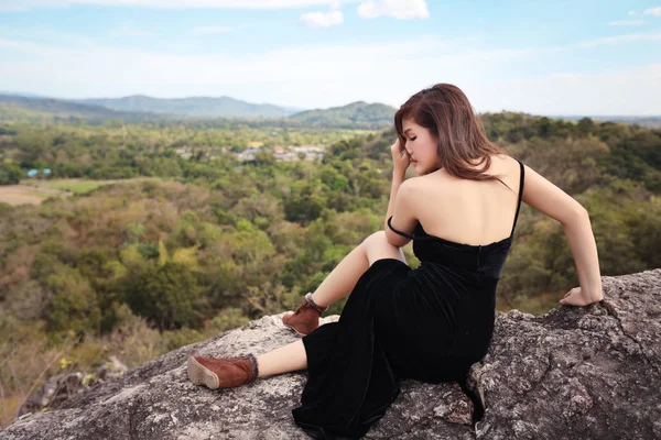 Tatil tatili sırasında dağda huzurlu doğada oturan siyah elbiseli genç asyalı kadının arka görünümü — Stok fotoğraf